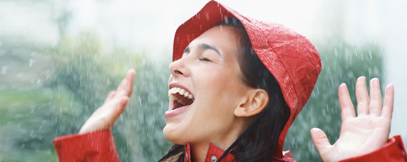 Lachende vrouw met regenkleding aan staat buiten in de regen