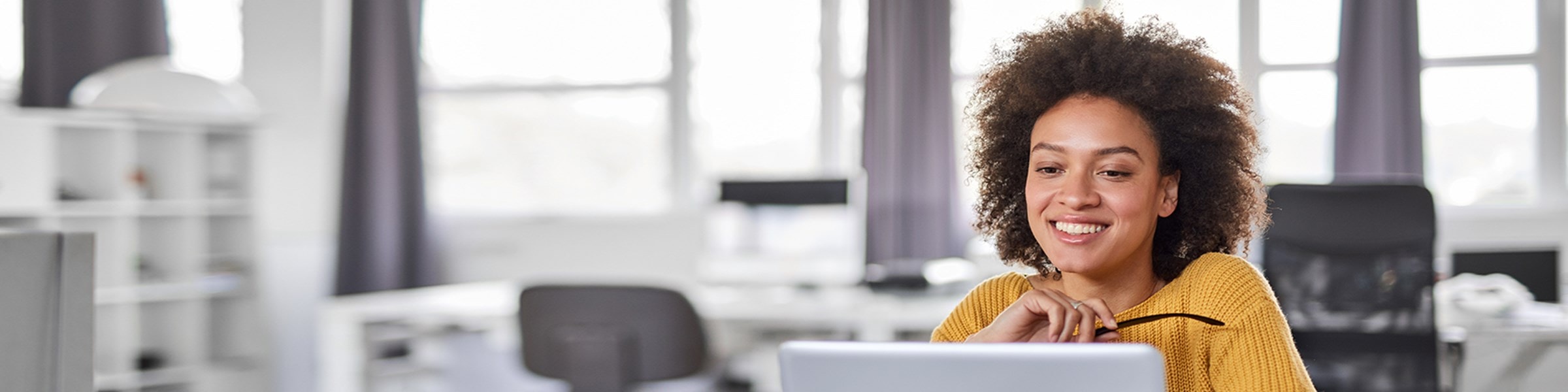 Vrouw aan bureau kijkt lachend naar haar scherm
