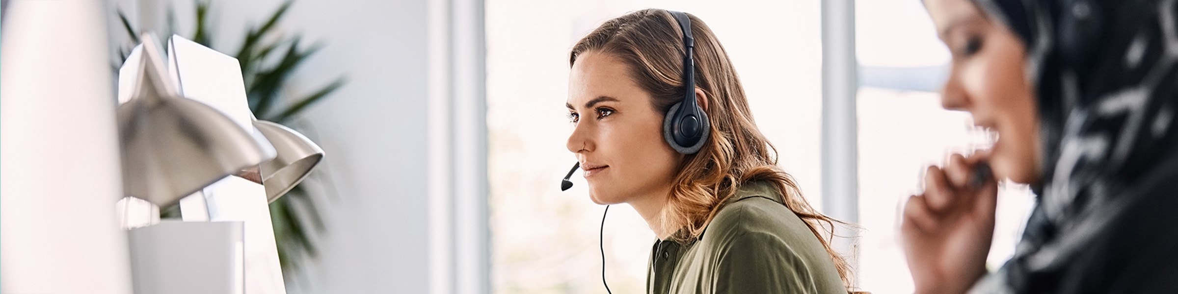 Twee jonge vrouwen met een headset op, die aan het werk zijn achter hun computer