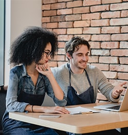 Vrouw en man zitten aan een tafel bekijken iets op laptop