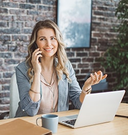 Vrouw zittend aan tafel met laptop is aan het telefoneren
