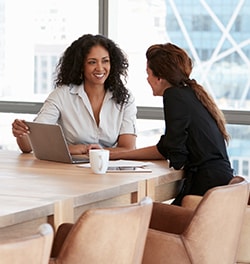 2 vrouwen overleggen aan tafel achter een laptop