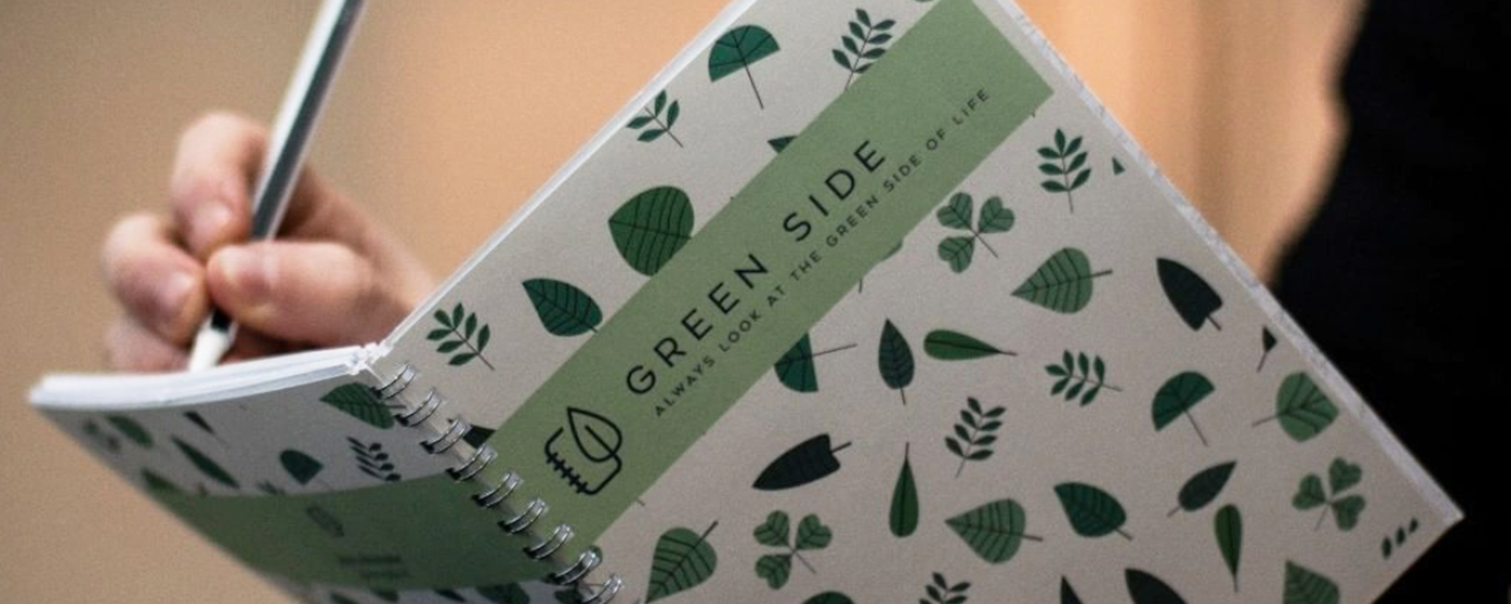 Een zichtbare hand die schrijft in een Green Site notitieboek | Upcycling oud papier | Dit is de tijd van doen | a.s.r.