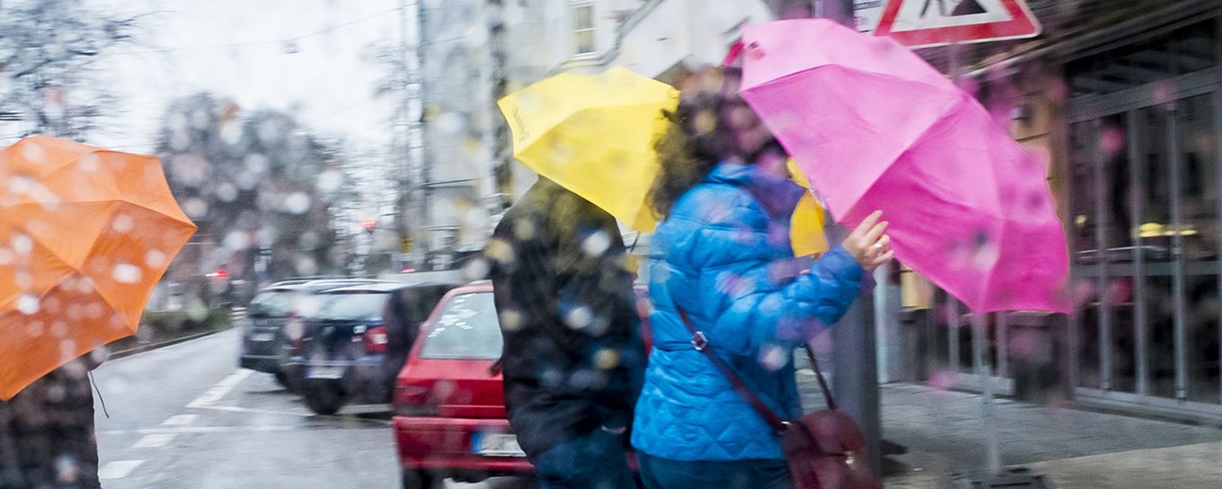 Mensen lopen in een straat met auto's en houden paraplu vast tegen de wind en de regen | tips tegen storm | a.s.r.