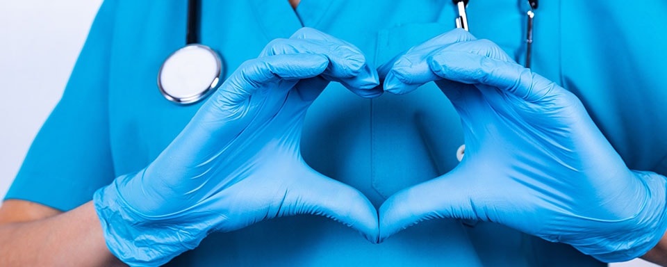 Verpleegster met blauwe handschoenen maakt een hart met haar handen | Dit is de tijd van doen | a.s.r.