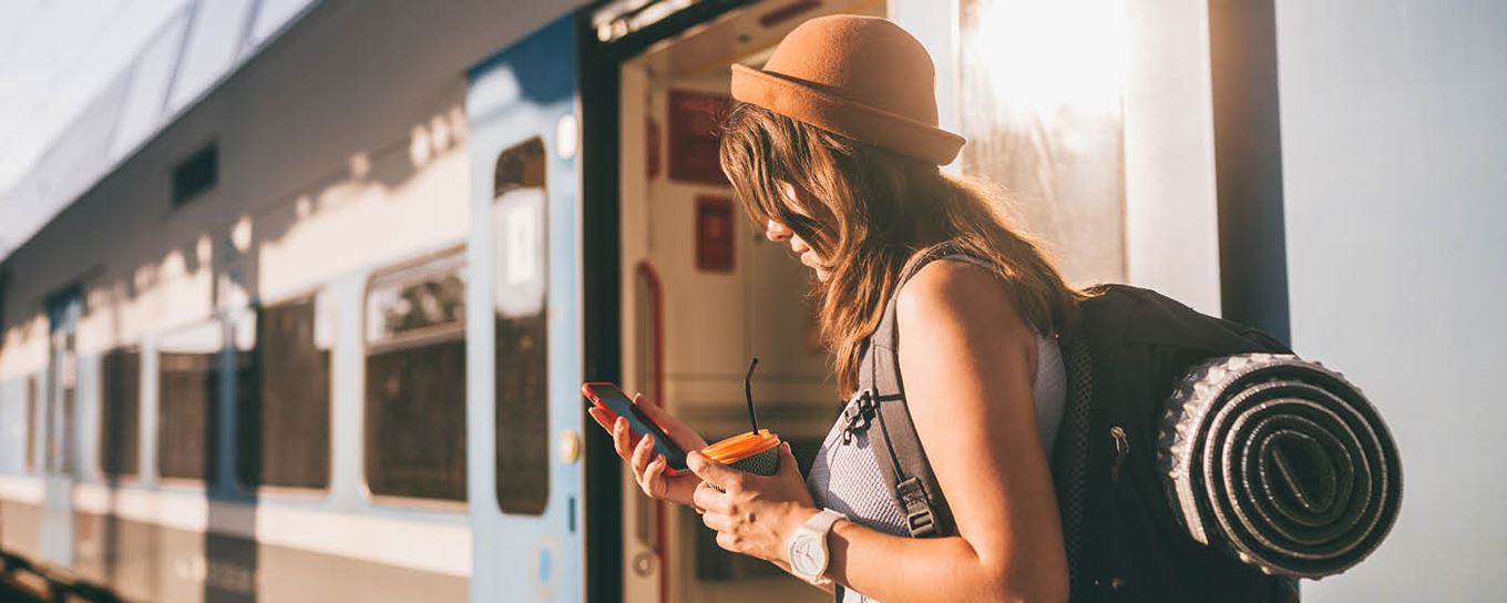 Jonge backpacker op het station checkt haar mobiele telefoon | a.s.r. | duurzaam vervoer | relaxed op vakantie
