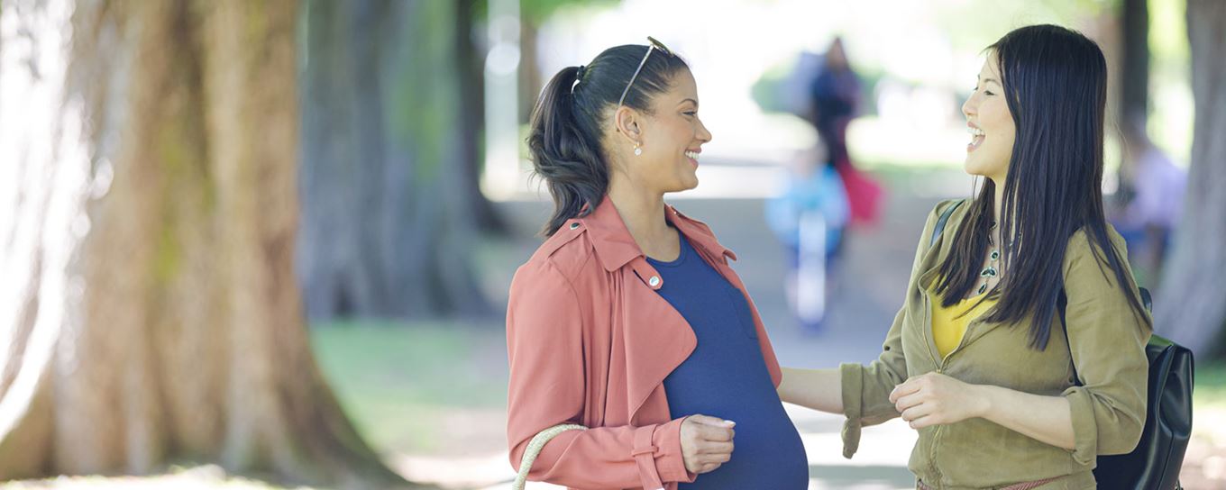 Twee vrouwen, waarvan een zwanger is, praten met elkaar op een pad met bomen | zwangerschap en veerkracht | a.s.r.