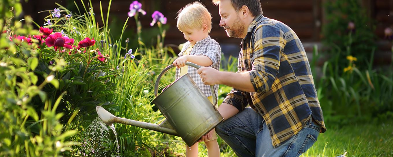 Vader en zoontje geven planten water met een ouderwetse gieter | a.s.r.