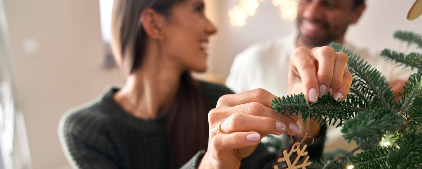 Vrouw hangt kerstviering in een kerstboom en praat met een man die achter haar staat