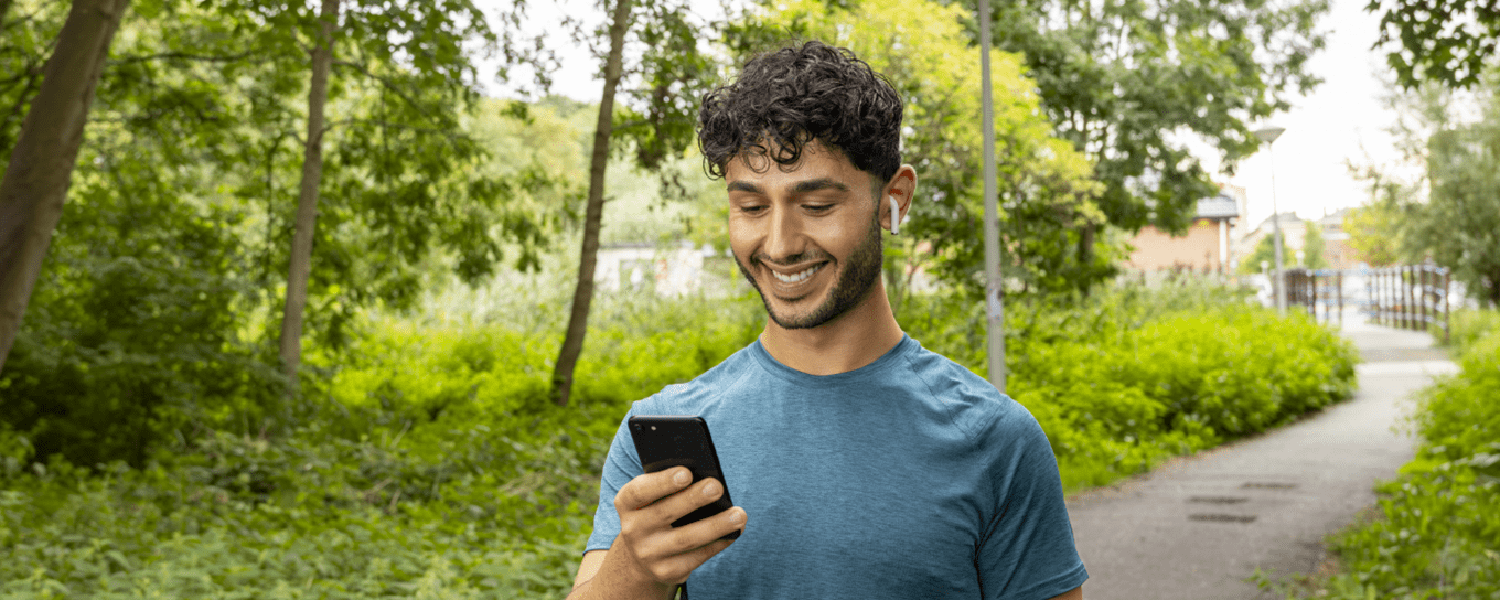 Jongeman kijkt op zijn smartphone tijdens het wandelen en hardlopen in het bos