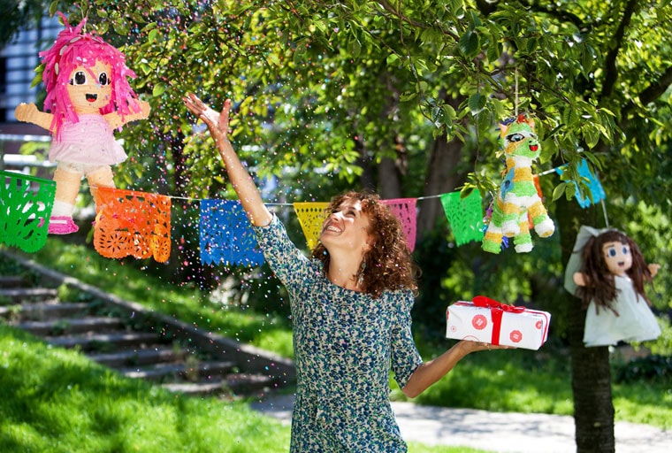 Katja Schuurman houdt in 1 hand een ingepakt cadeautje en gooit confetti weg met de andere.