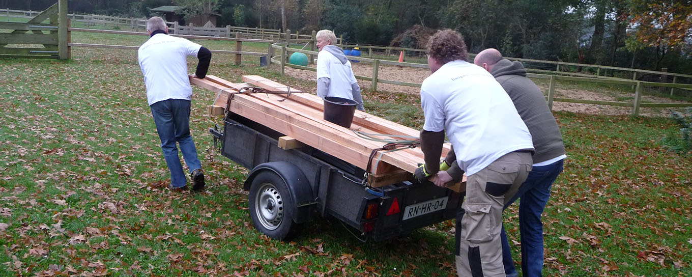 a.s.r. vrijwilligers verplaatsen houten balken met een aanhangwagen