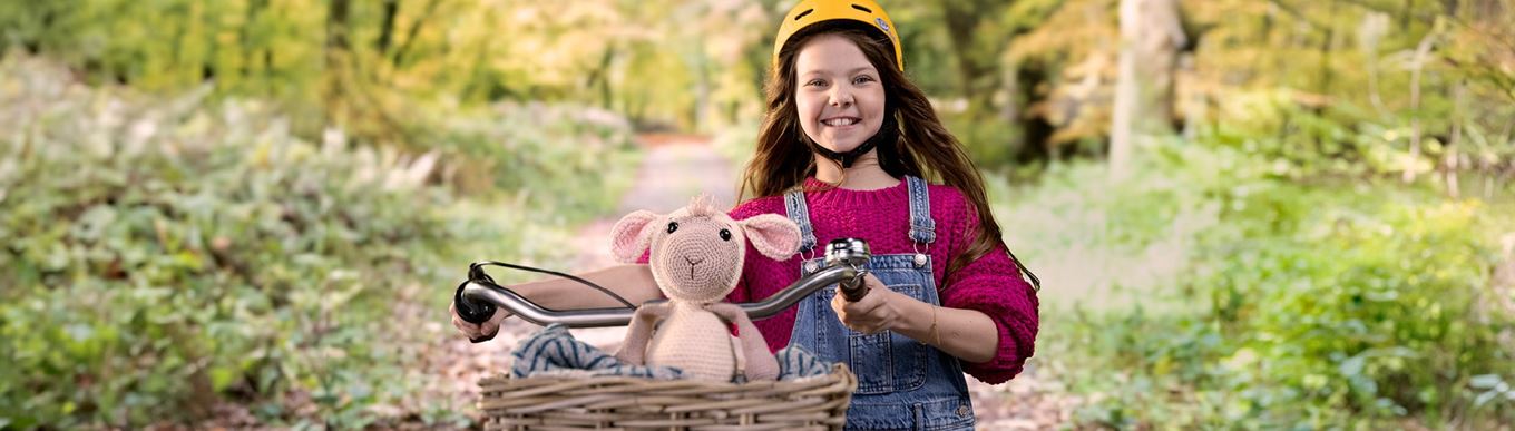 jong meisje met bruin haar kijkt lachend in camera. In haar fietsmandje zit een knuffel die herstelt is