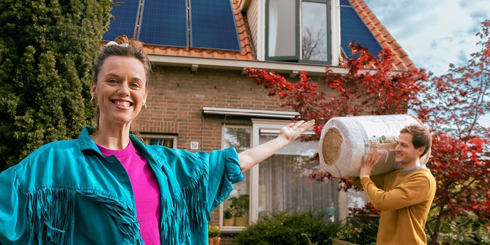 Twee mensen staan voor een huis. De man draagt een rol isolatie materiaal op zijn schouder.