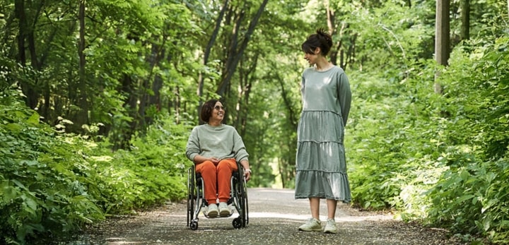vrouw in een rolstoel en een andere vrouw naast haar wandelend in het bos