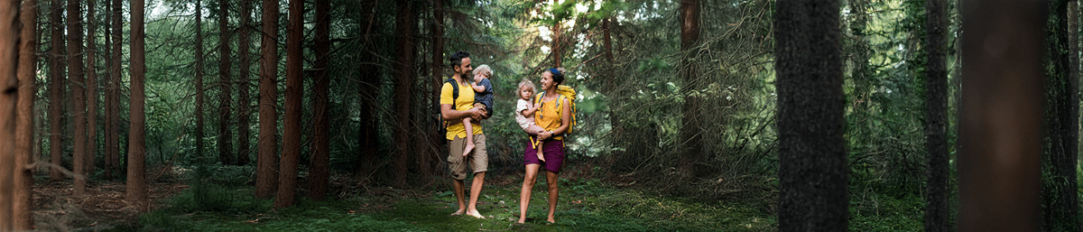 man vrouw en twee kinderen op hun armen op blote voeten wandelend door het bos