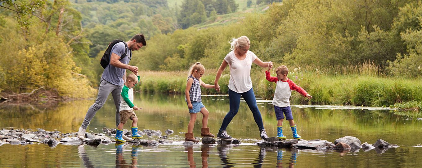 een gezin met 3 kinderen proberen een beekje over te steken over stenen 