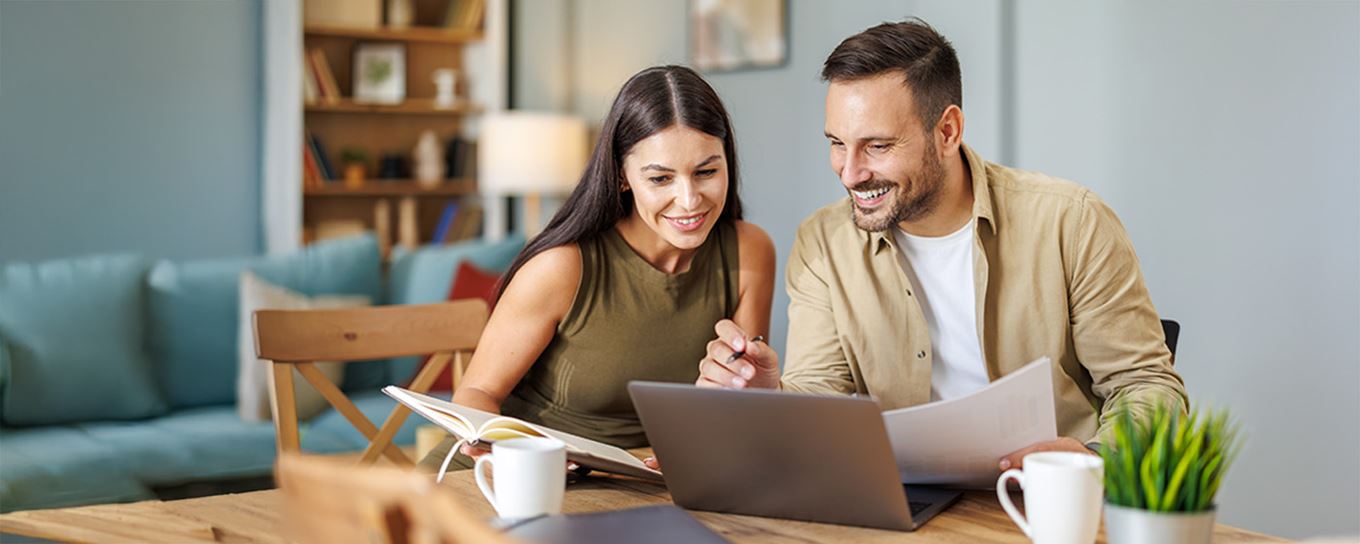 Een jongeman en jonge vrouw zitten samen aan de eettafel met een laptop en hun belangrijke papieren om iets in te vullen op de laptop