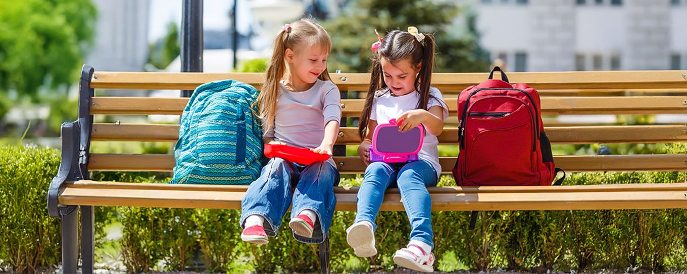 twee meisjes zittend op een bankje en openen hun lunchtrommel
