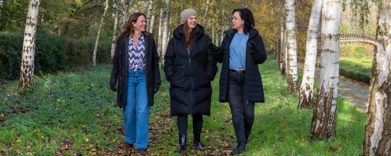 3 vrouwen lopen al wandelend met elkaar door het bos