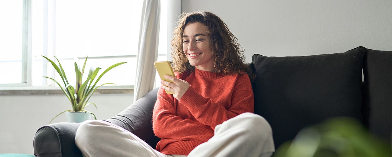 Jong meisje zittend op de bank kijkend naar haar mobiel