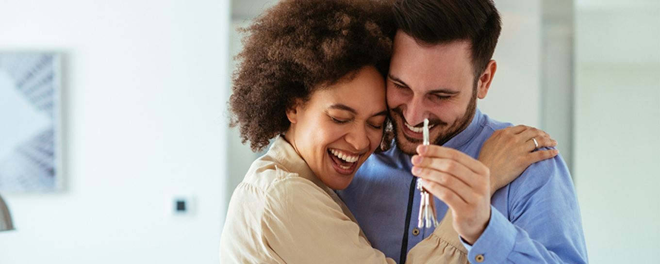 man en vrouw knuffelen elkaar blij met hun sleutels in de handen van het nieuwe huis