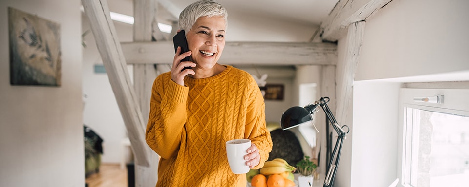 Blije vrouw met kop koffie in de hand aan de telefoon in een thuissituatie