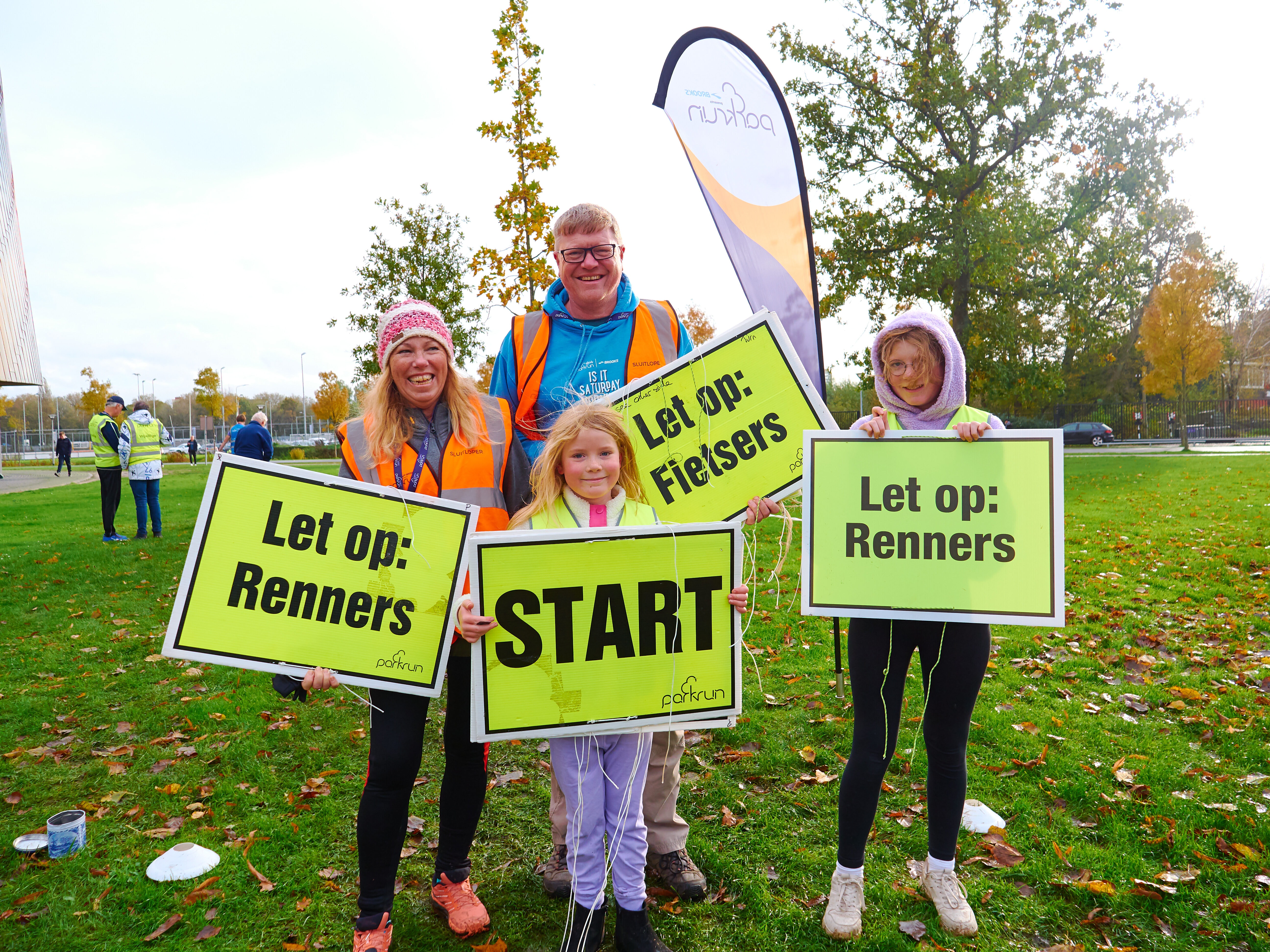 Man, vrouw en twee kinderen lachend met bordjes bij parkrun 